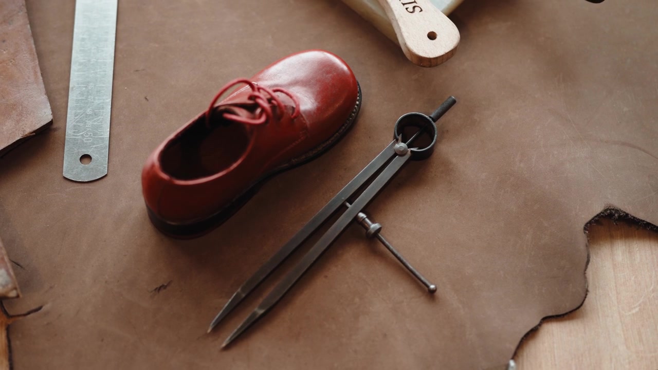 Roter Kinderschuh mit Schnürsenkeln neben Stahlteilern und Lineal auf einer braunen gemusterten Platte