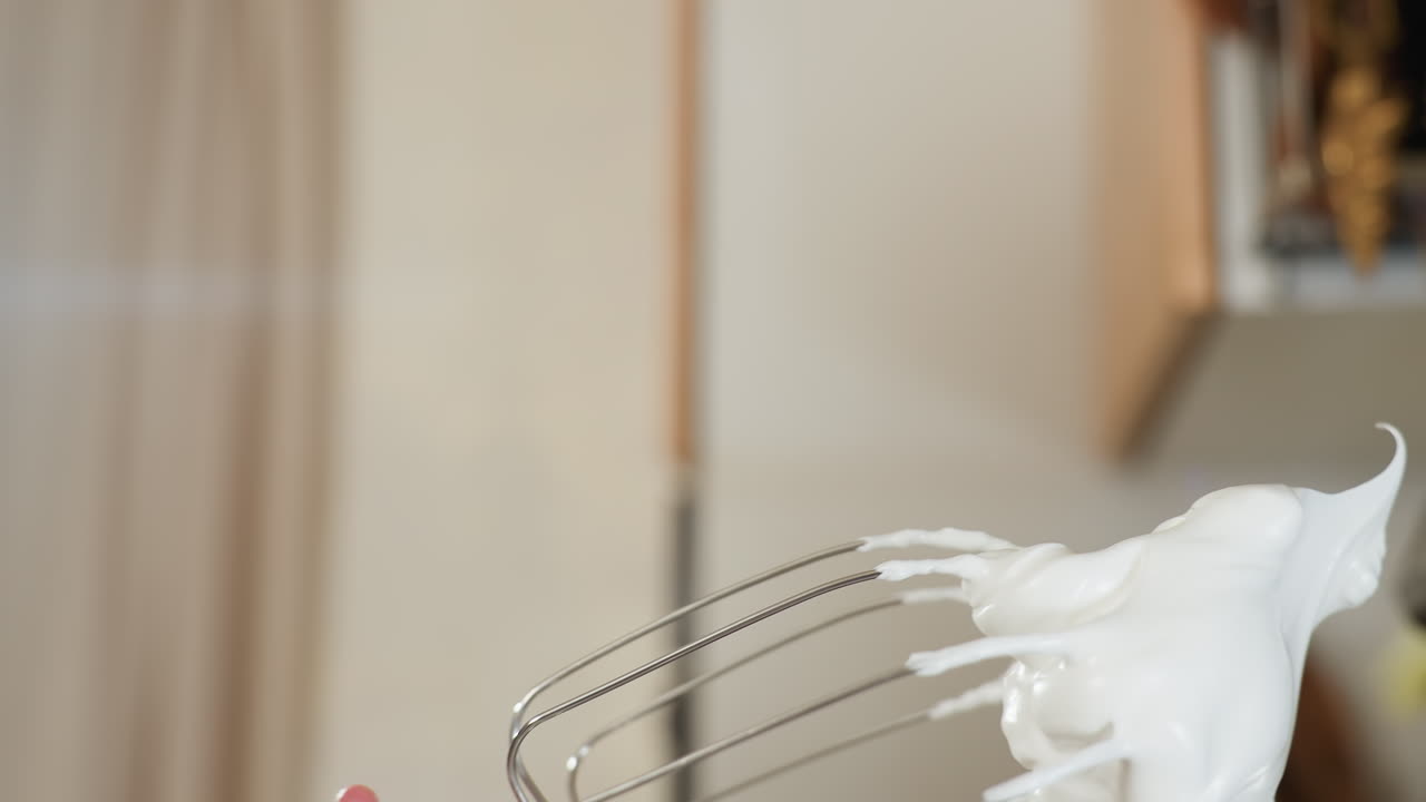 Close up of stainless steel mixer beater coated with thick whipped cream or meringue showing smooth texture and glossy peaks, ideal for baking