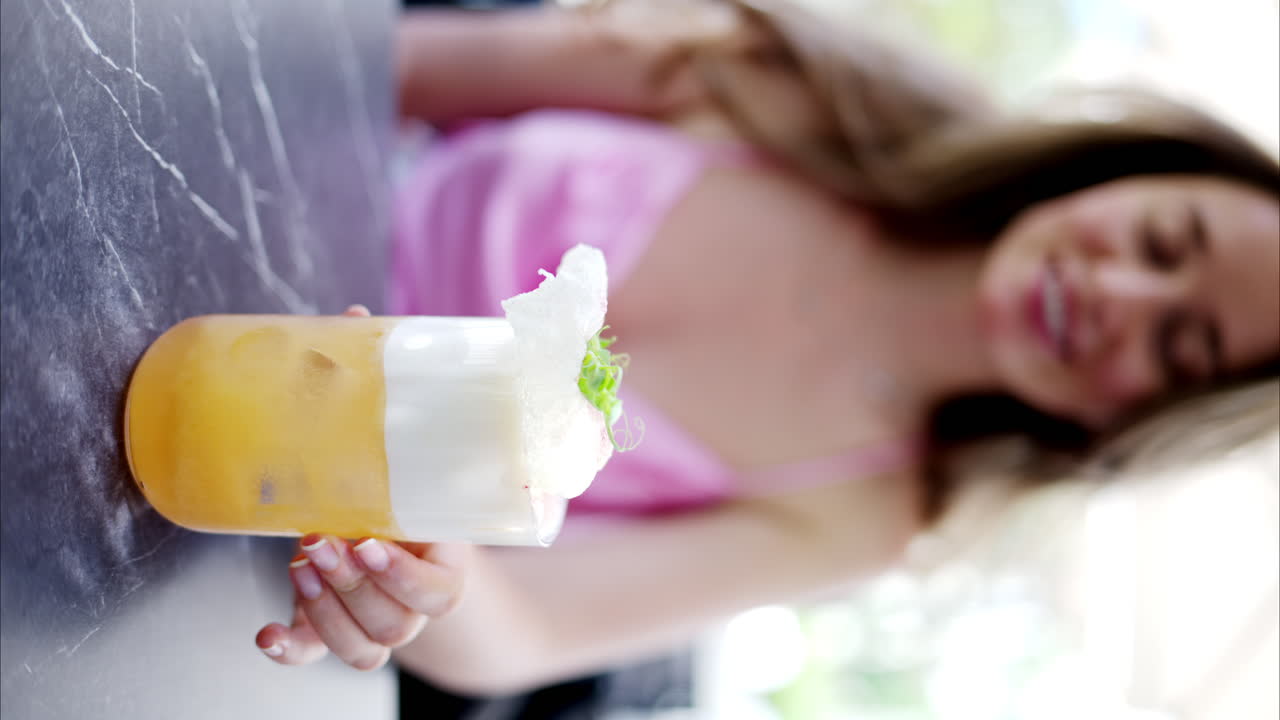 Woman holding a summer white and orange cocktail with whiskey and peach juice, slow motion vertical screen