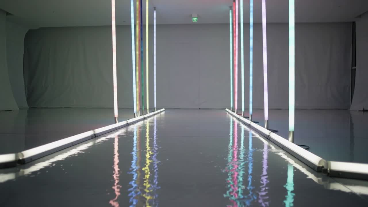 Tubi verticali e barre a pavimento che si muovono mostrando sottili cambiamenti e riflessi increspati in galleria.