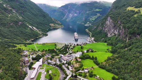 Vista-Aérea-Del-Pintoresco-Fiordo-De-Geiranger-Y-Crucero-Anclado-Por-El-Pueblo-Y-Las-Verdes-Colinas,-Noruega