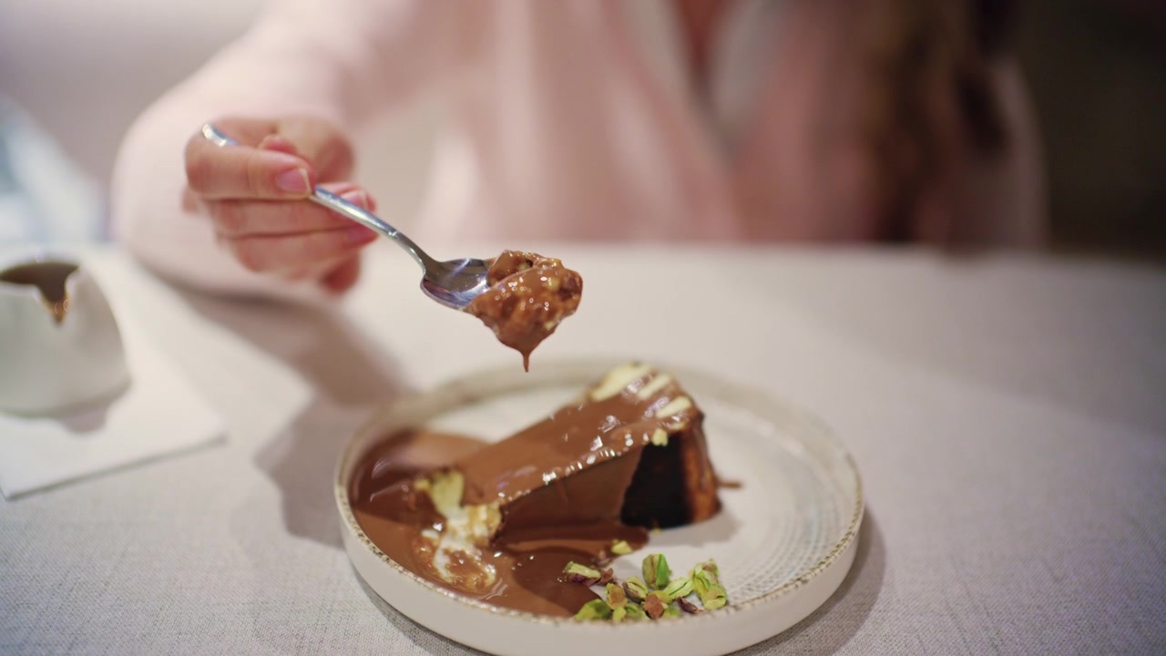 Primo piano di una donna che mangia una fetta di cheesecake al forno generosamente ricoperta di salsa al cioccolato fuso