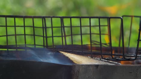 burning wood an coals in rusty portable outdoor bbq grill in sunny day, close up shot