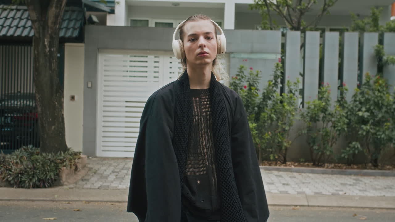 Chic Serious Male Zoomer in Black Clothes Wearing Headphones Outdoors