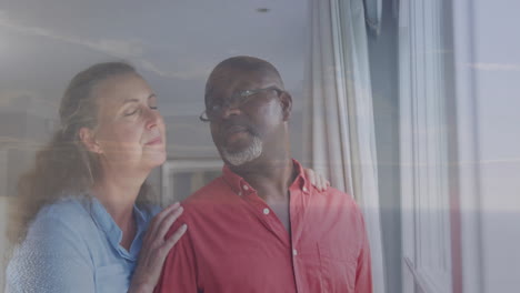 standing by window, older couple looking outside thoughtfully, sharing quiet moment