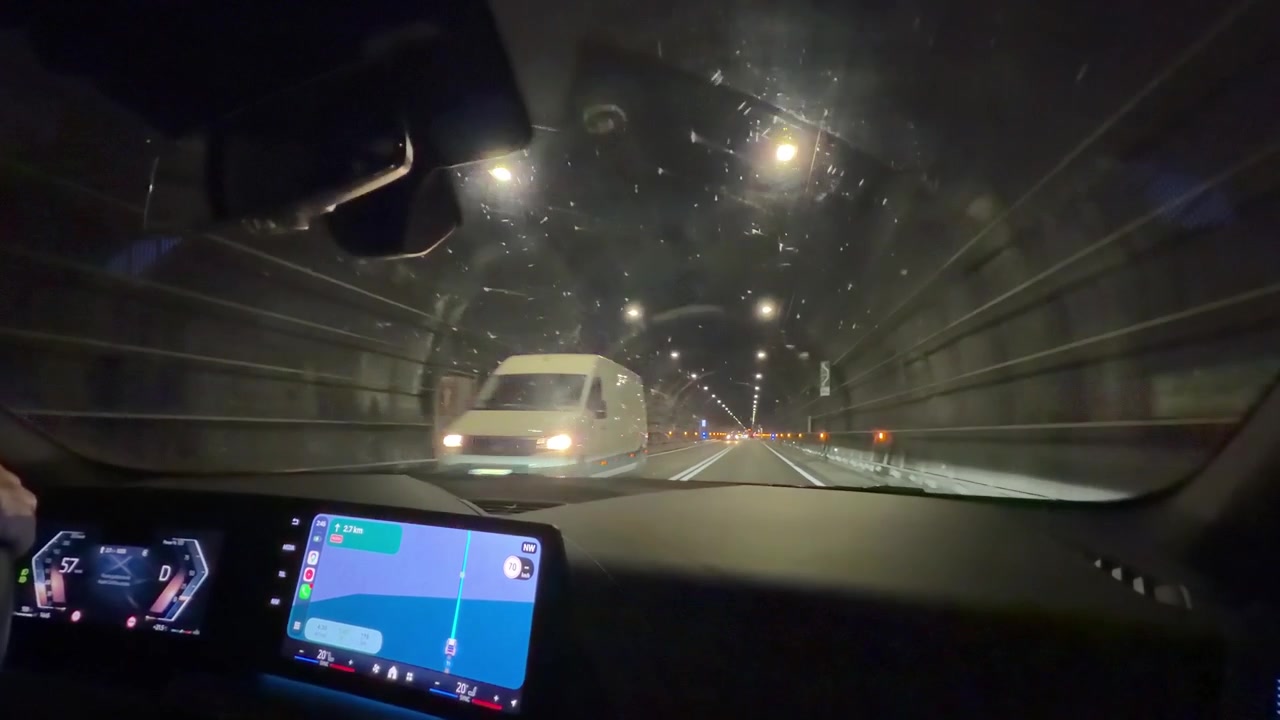 Vista do interior do carro dirigindo por um túnel de montanha iluminado à noite com navegação GPS ativa.