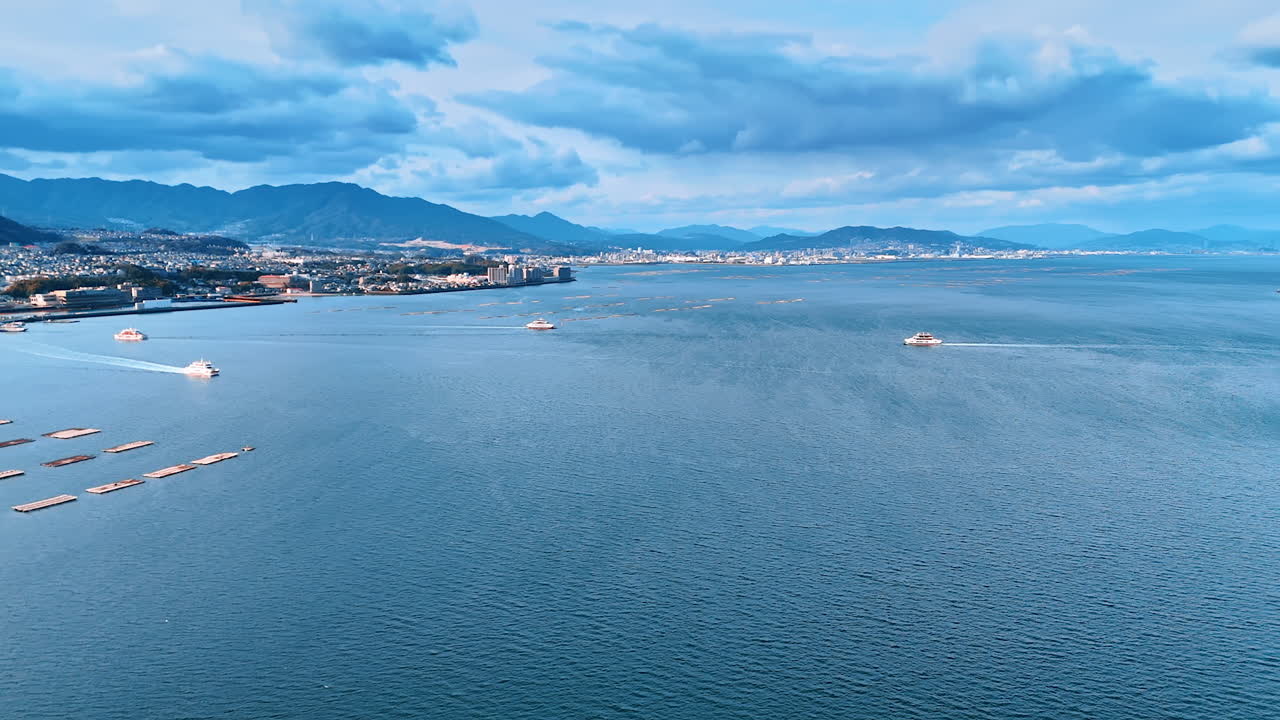 Motor boats cross the splendid azure waterscape of the Inland Sea in Japan. Drone footage above the scenery revealing view on the oyster farm located on the water.