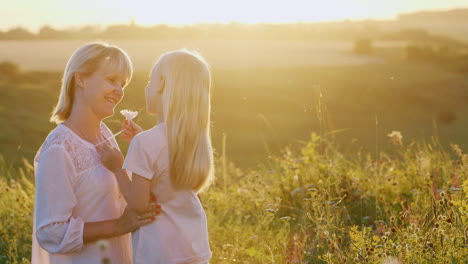 two blond mother and daughter communicate with each other on the green lawn against the backdrop of