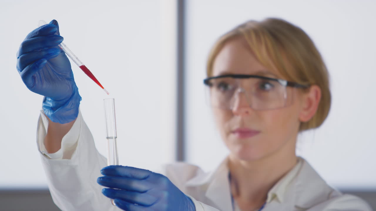 Tecnica di laboratorio che indossa un camice bianco e aggiunge liquido rosso da una pipetta in una provetta