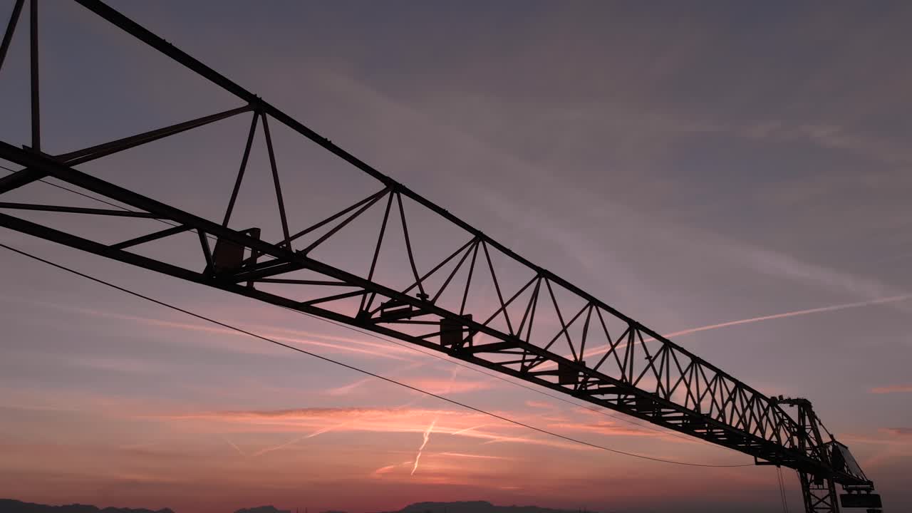 Drone fly close to tower crane excavator during sunset in a construction site. Silhouette close up view colorful sky