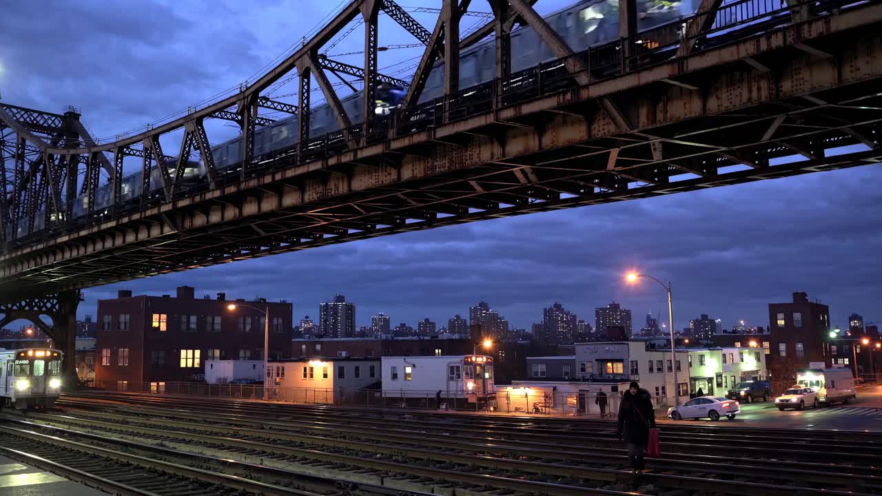 A low-angle video shot captures a train crossing a bridge at dusk, with city lights and tracks
