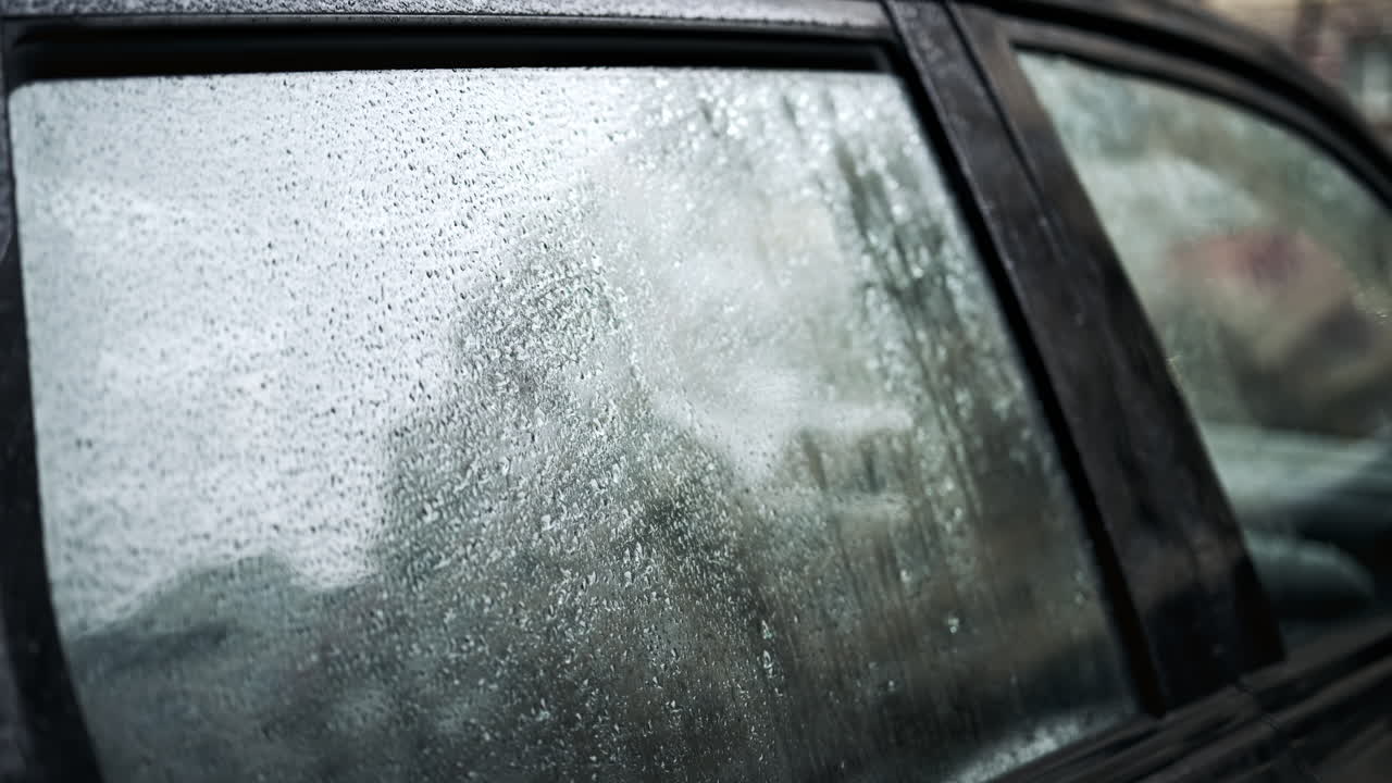 Primo piano di gocce di pioggia che coprono il finestrino dell'auto con sfondo urbano sfocato