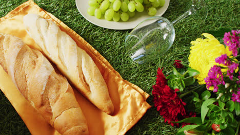 Video-of-fresh-bread,-grapes-and-wine-on-blanket-and-gingham-tablecloth-with-copy-space-on-grass