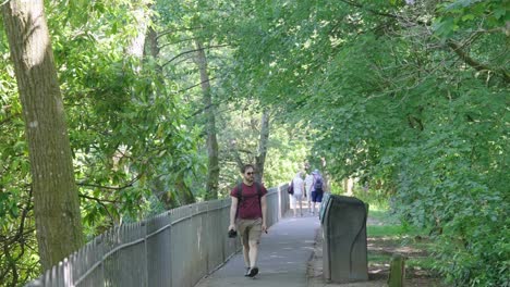 man wearing sunglasses carrying a camera walking along a public path