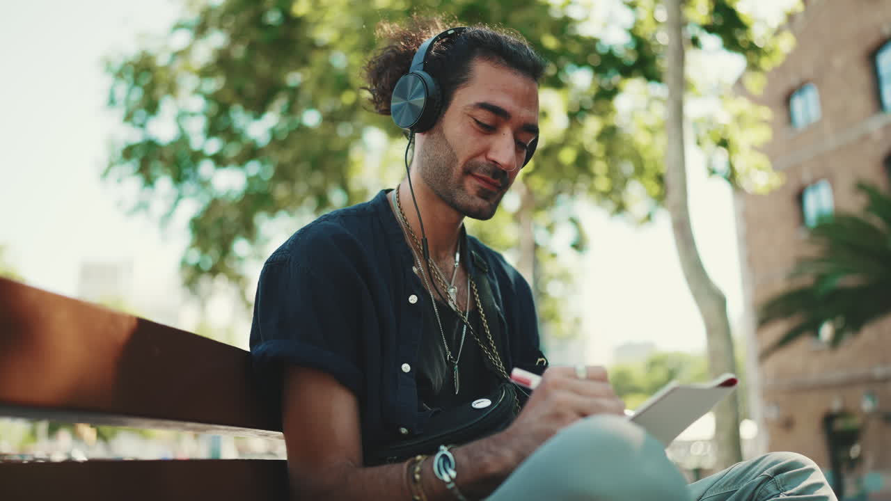 Uomo con cuffie che scrive su un quaderno al parco