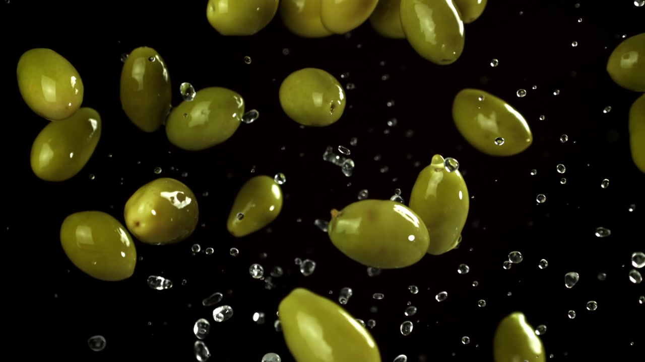 Olive verdi con goccioline d'acqua che schizzano su sfondo nero al rallentatore
