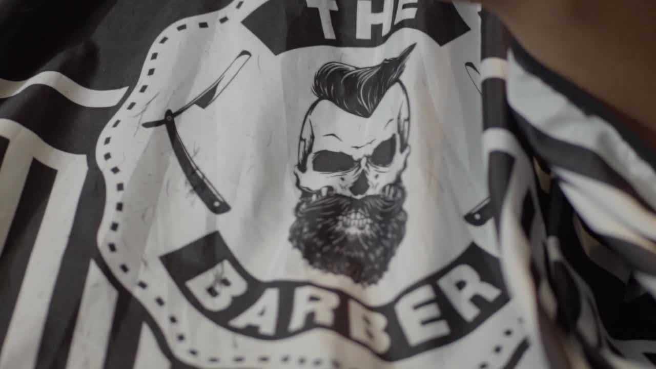 Close-up of a barber cape with a skull logo, scissors, and a straight razor design