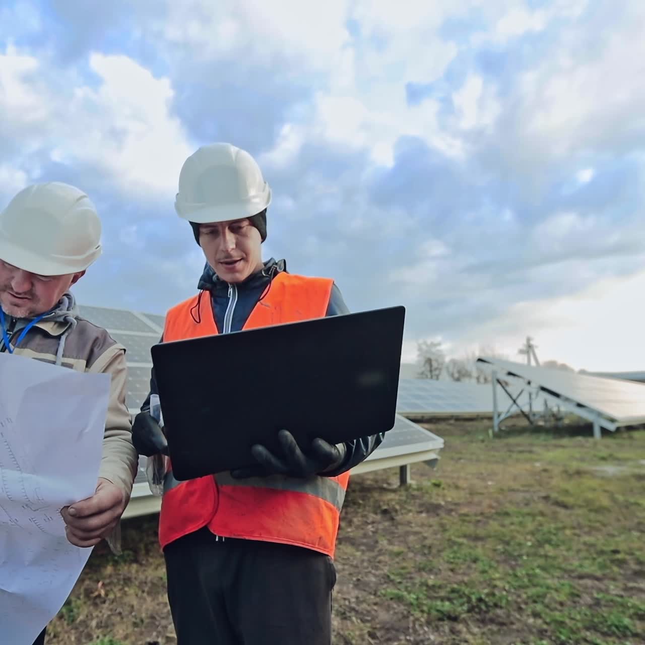 Technicians with plan and laptop on the solar farm. Workers in special uniform discussing the construction of solar panels to get clean energy.