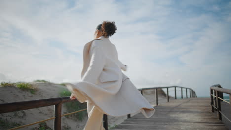 Gorgeous-woman-open-arms-walking-pier.-Cheerful-curly-african-american-spinning