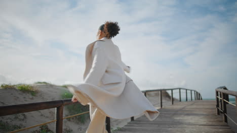 Gorgeous woman open arms walking pier. Cheerful curly african american spinning