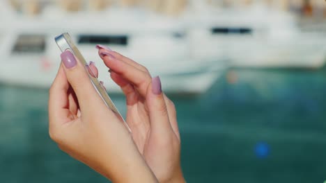 manos femeninas con teléfono sobre un fondo de un plan borroso con el mar y los yates siempre conectados