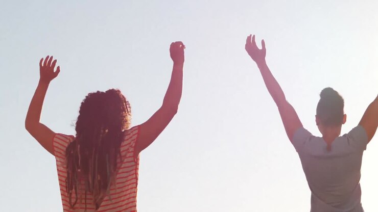 Coppia lesbica felice che alza le mani all'aperto in una giornata di sole