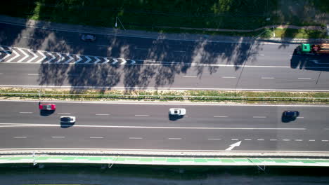 Cars-exit-on-off-ramp-under-shade-of-trees,-cars-commute-across-open-non-crowded-highway,-aerial-top-down-perspective