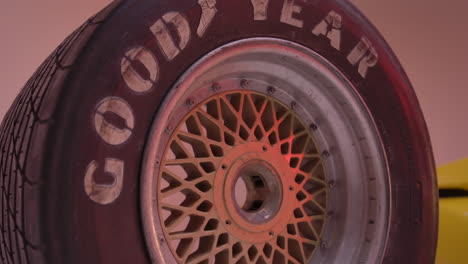 4k huge truck tire standing on top of another tire with golden rims in a red lit studio