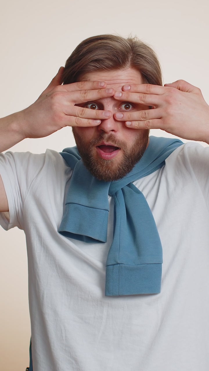 Neugieriger kaukasischer Mann, der sich die Augen mit der Hand verdeckt und durch die Finger späht, sich versteckt und hervorlugt