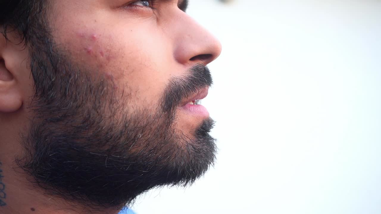 Uomo indiano barbuto che fuma profondamente una sigaretta su sfondo isolato ad Agra, India - Primo piano