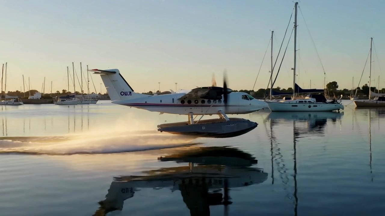 Pilot gibt Gas, ein zweimotoriges Wasserflugzeug gleitet mit Schwimmern in der tief stehenden Sonne über den Yachthafen zum Start.