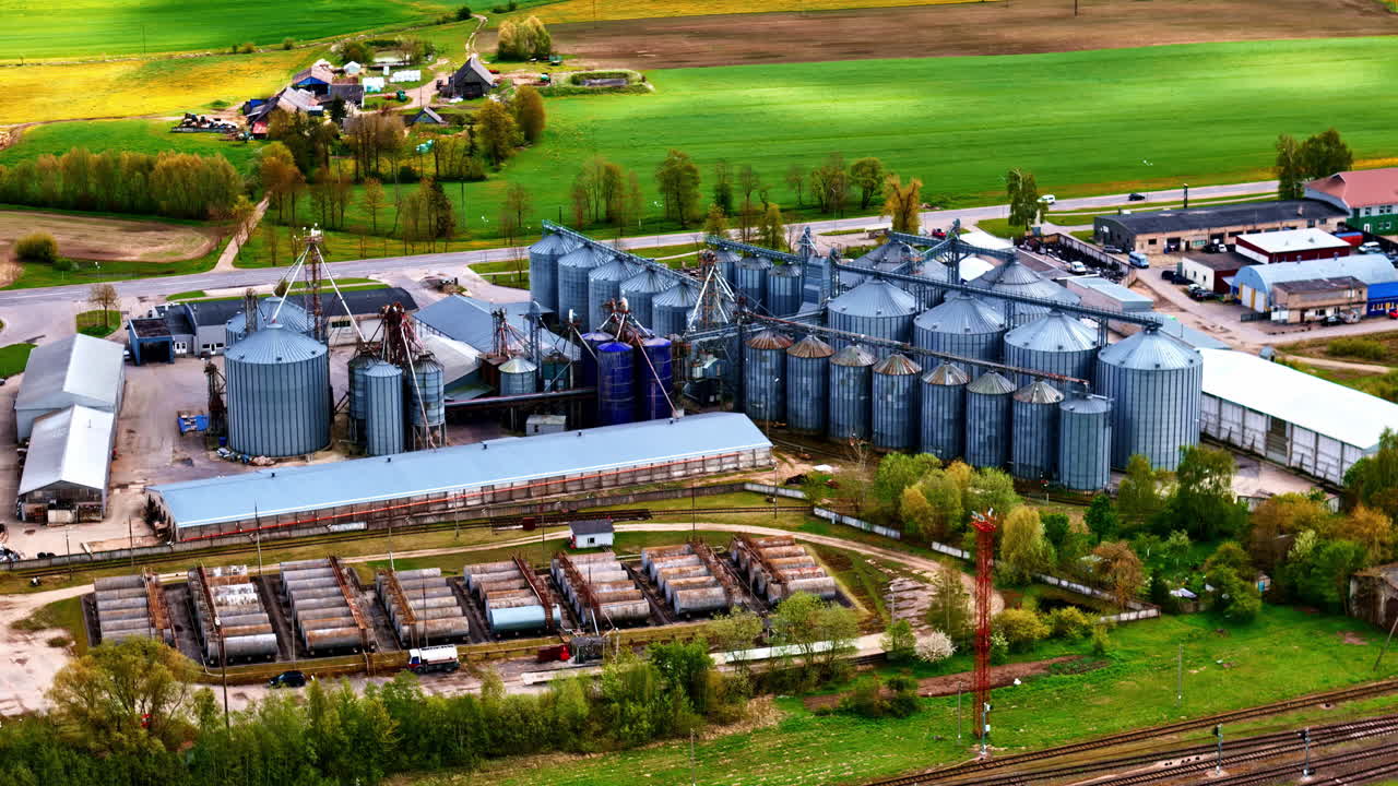 Silos and roads stretch across green plain with equipment in neat agricultural plots