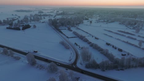 aerial establishing shot of a rural landscape, countryside roads, agricultural fields and trees covered with snow, cold freezing weather, sunset golden hour light, wide drone shot moving forward high