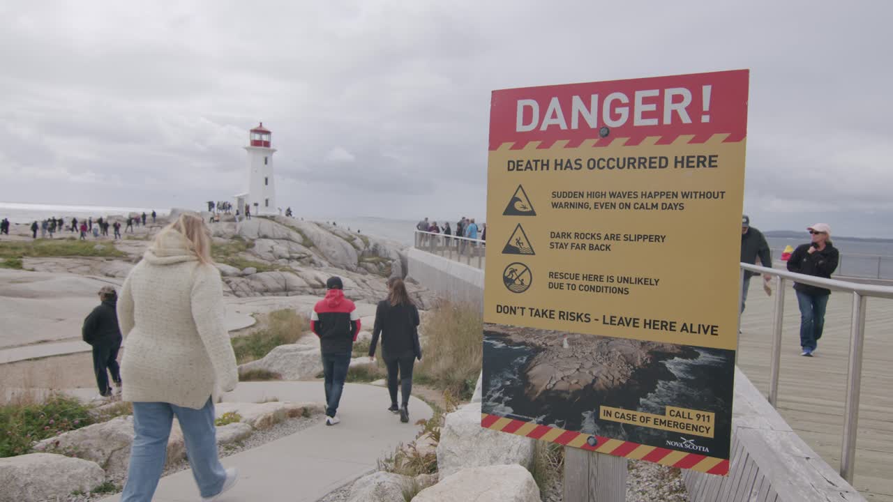 Warning sign at Peggys Cove lighthouse, cautioning visitors about dangerous waves and slippery rocks