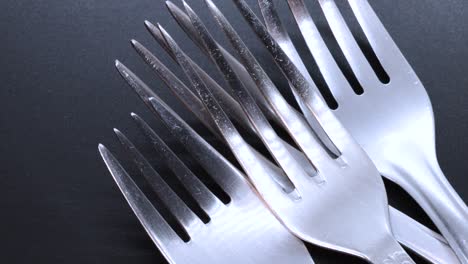 Macro-shot-of-four-steel-forks-on-a-black-bacground,-rotating-motion