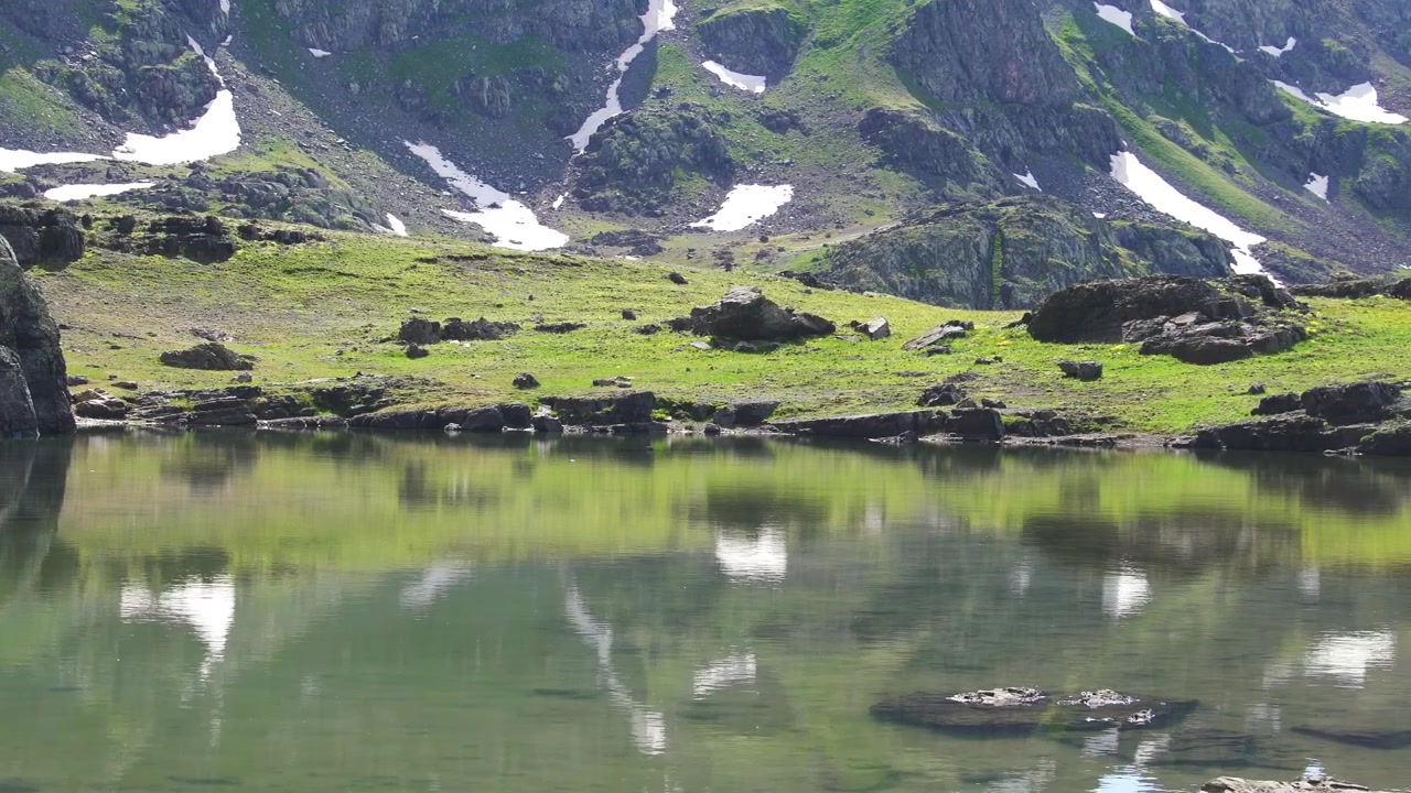 Rolig alpesjø som speiler snødekte fjell.