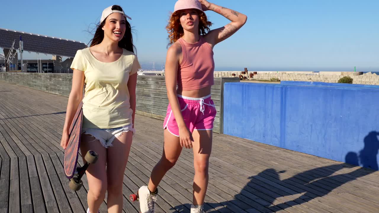 Two women walking with skateboard on boardwalk