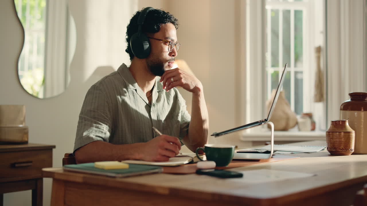 Young Man Working and Writing in Home Office with Laptop and Headphones