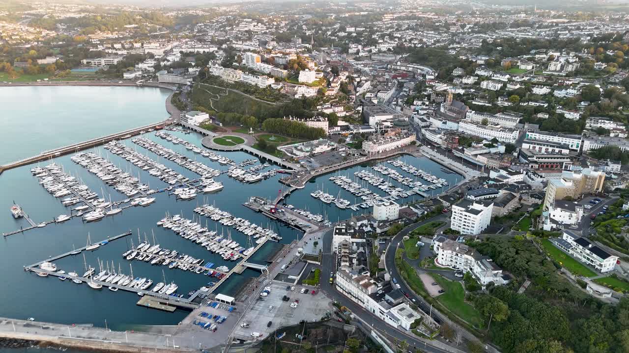 Cinematic aerial drone footage tracking and panning left over Torquay Marina showcasing boats yachts docked in harbor with waterfront buildings and coastal town in Devon England