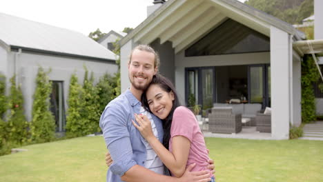 a young biracial couple embraces lovingly in their backyard