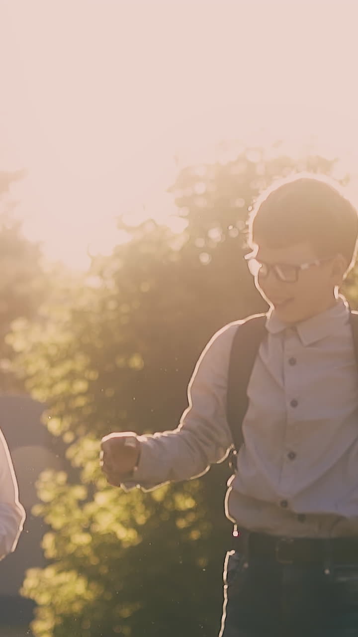 happy schoolboys with red and black bags throw books after passing exam and give high five at back sunlight slow motion