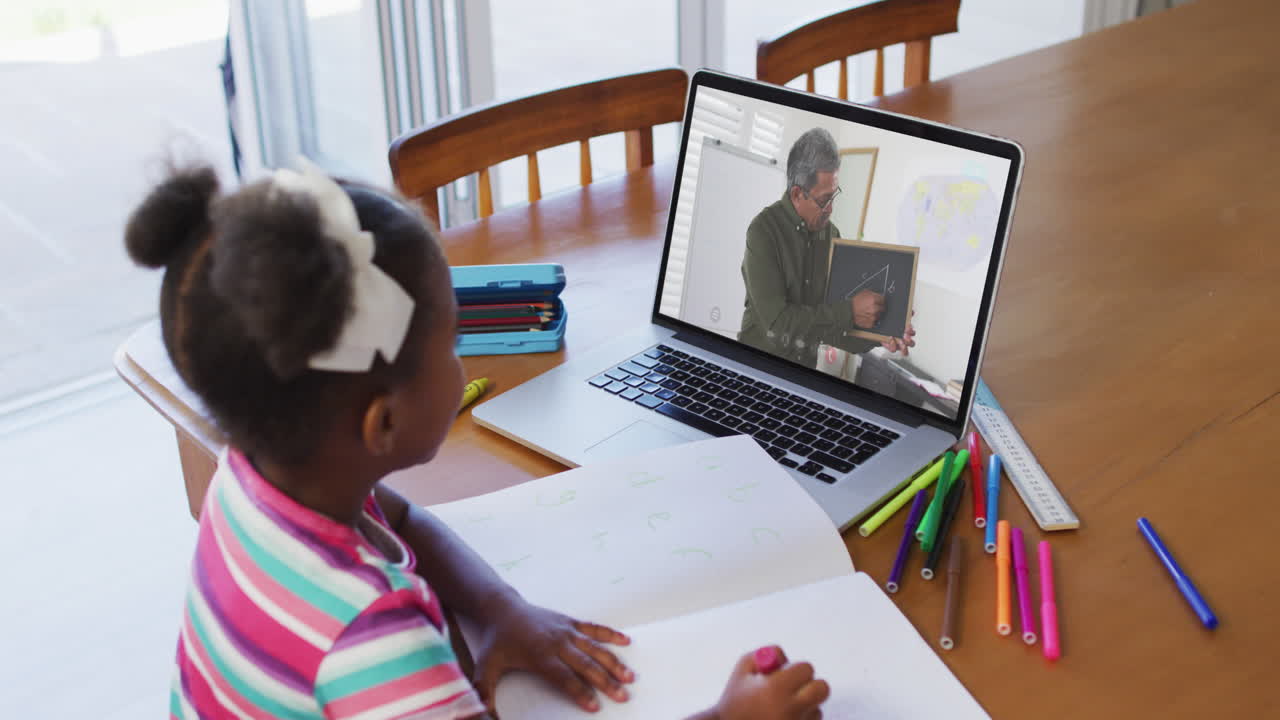 African american girl doing homework while having video call with male teacher on laptop at home
