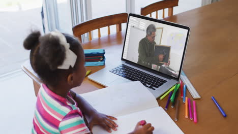 african american girl doing homework while having video call with male teacher on laptop at home