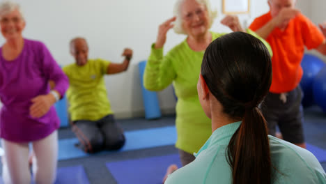 Rear-view-of-female-trainer-training-senior-people-in-exercise-at-fitness-studio-4k