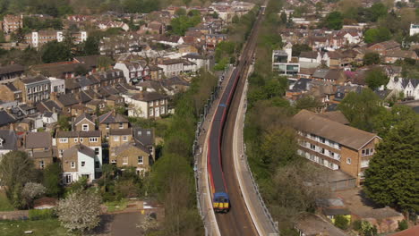 Passenger-train-stopping-at-train-station-in-Kingston-Upon-Thames,-aerial-orbit-cinematic-view