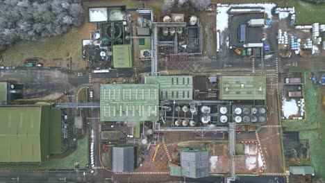 Overhead-cinematic-drone-aerial-footage-of-a-large-industrial-plant-showing-pipework-structures,-buildings,-cooling-towers,-steam,-and-work-vehicles