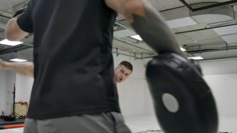 fighter strikes with a turn during the rotation of the leg. coach holds paws for kick-boxer training before fight