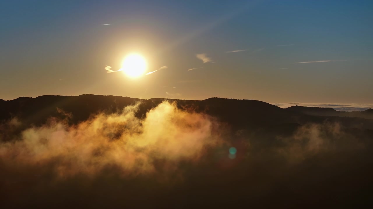 Sonnenaufgang über einem Berg mit großer leuchtender Nebelwolke im Vordergrund