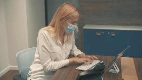 mujer de negocios joven con máscara facial escribiendo en la tableta en la oficina