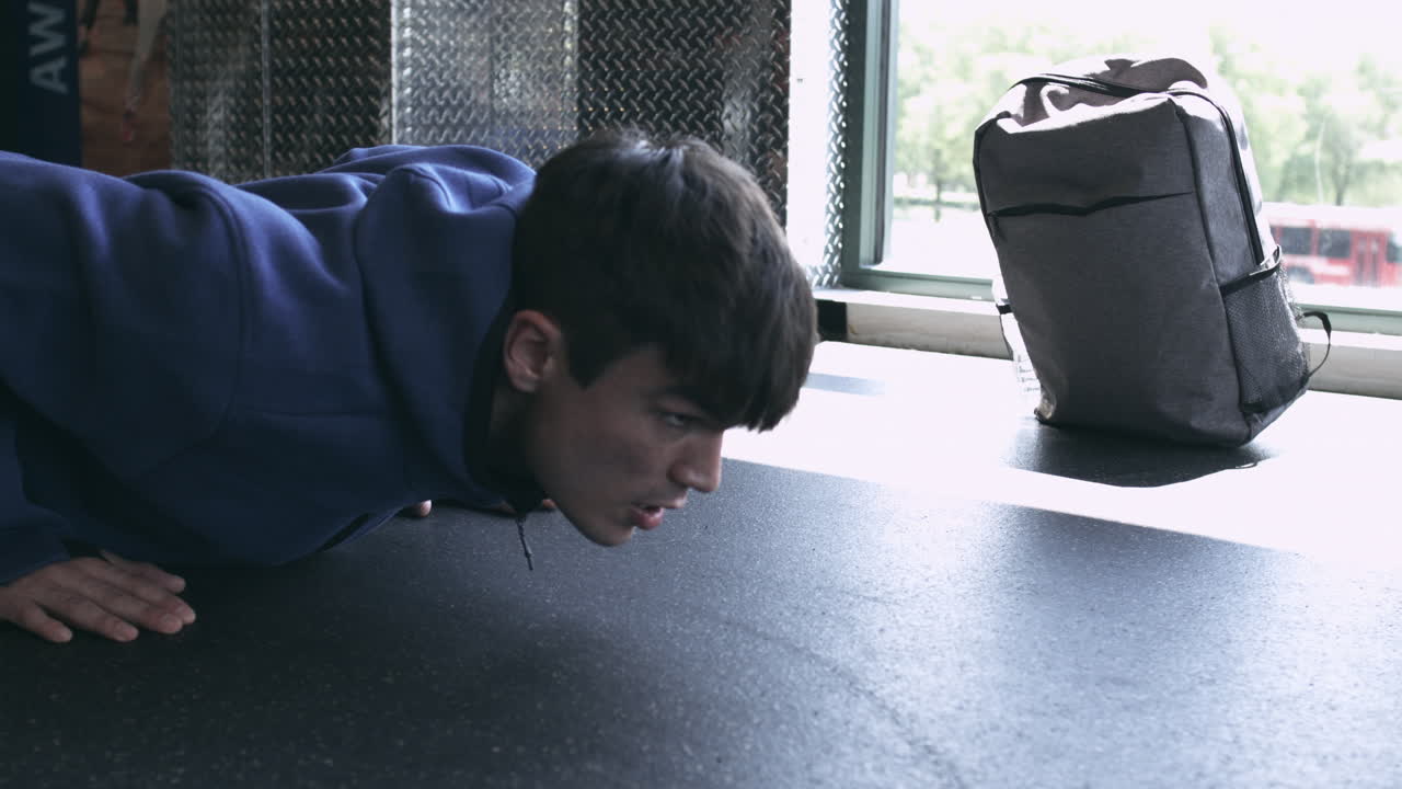 Millennial male doing push ups in the gym with his workout bag in the background stabilized shot in UHD 4K